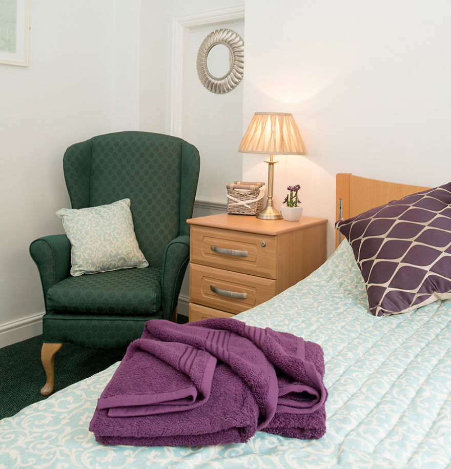 bedroom with green armchair, bedside table and purple towels