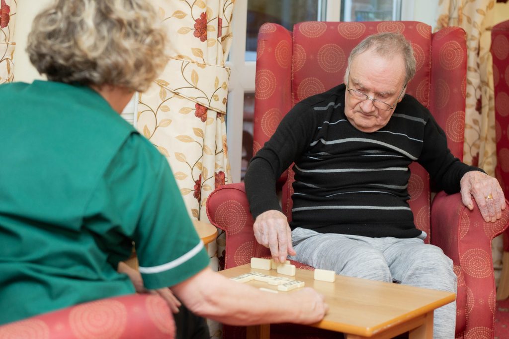 team member and male resident playing dominoes together
